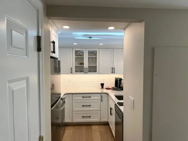 Bright white kitchen viewed through a doorway, with cabinets, stovetop, microwave, and light wood floor.
