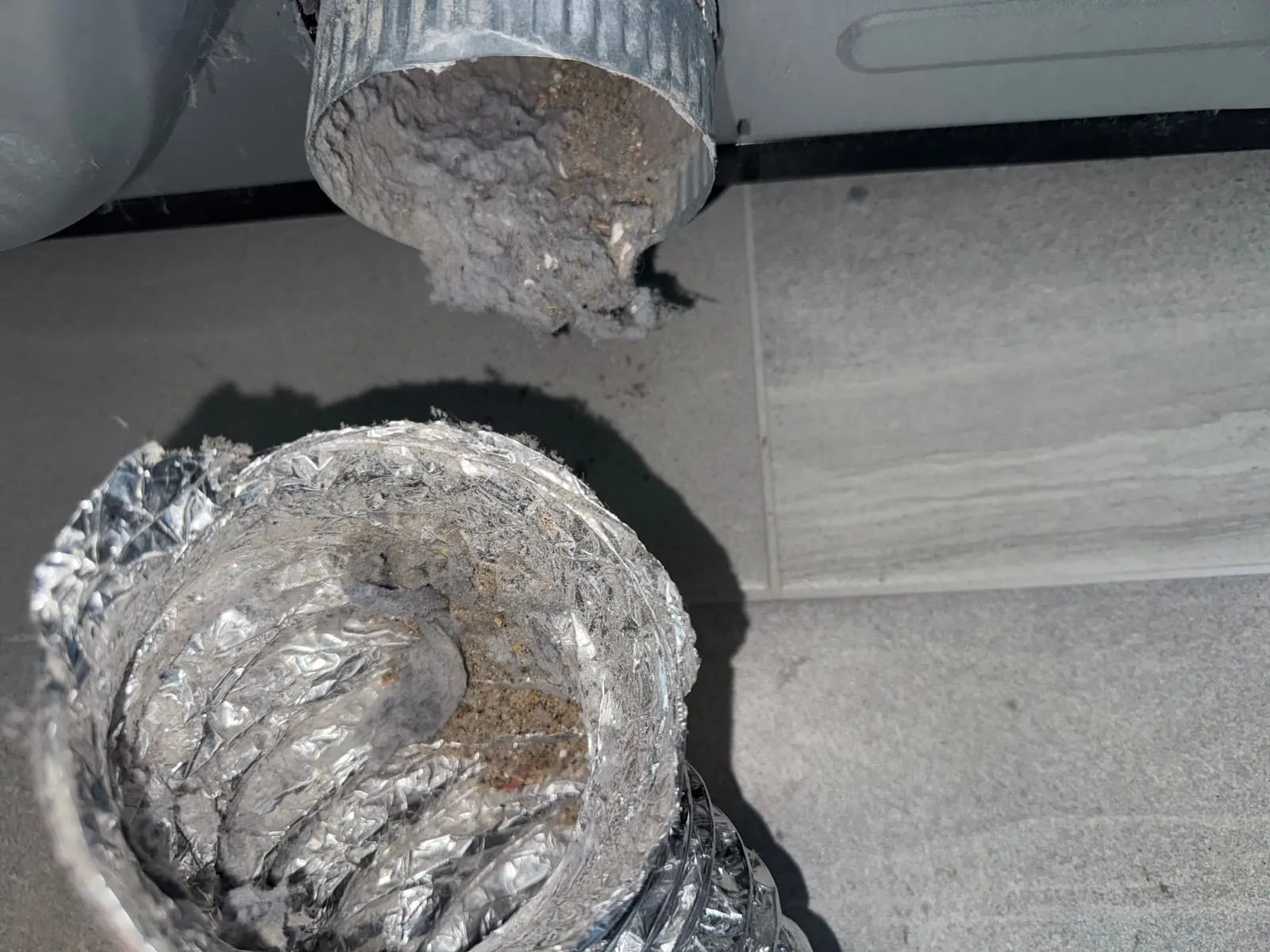 A section of dryer duct laid on the floor with its interior lined in compacted lint and grey debris.