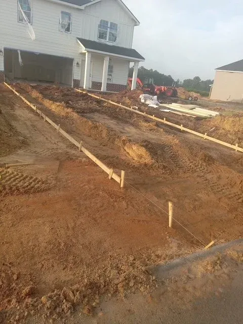 Driveway construction in progress in front of a residential house, with wooden framing and soil preparation.