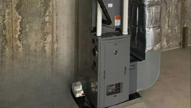 A gray furnace in a basement setting with ductwork and a white pipe.