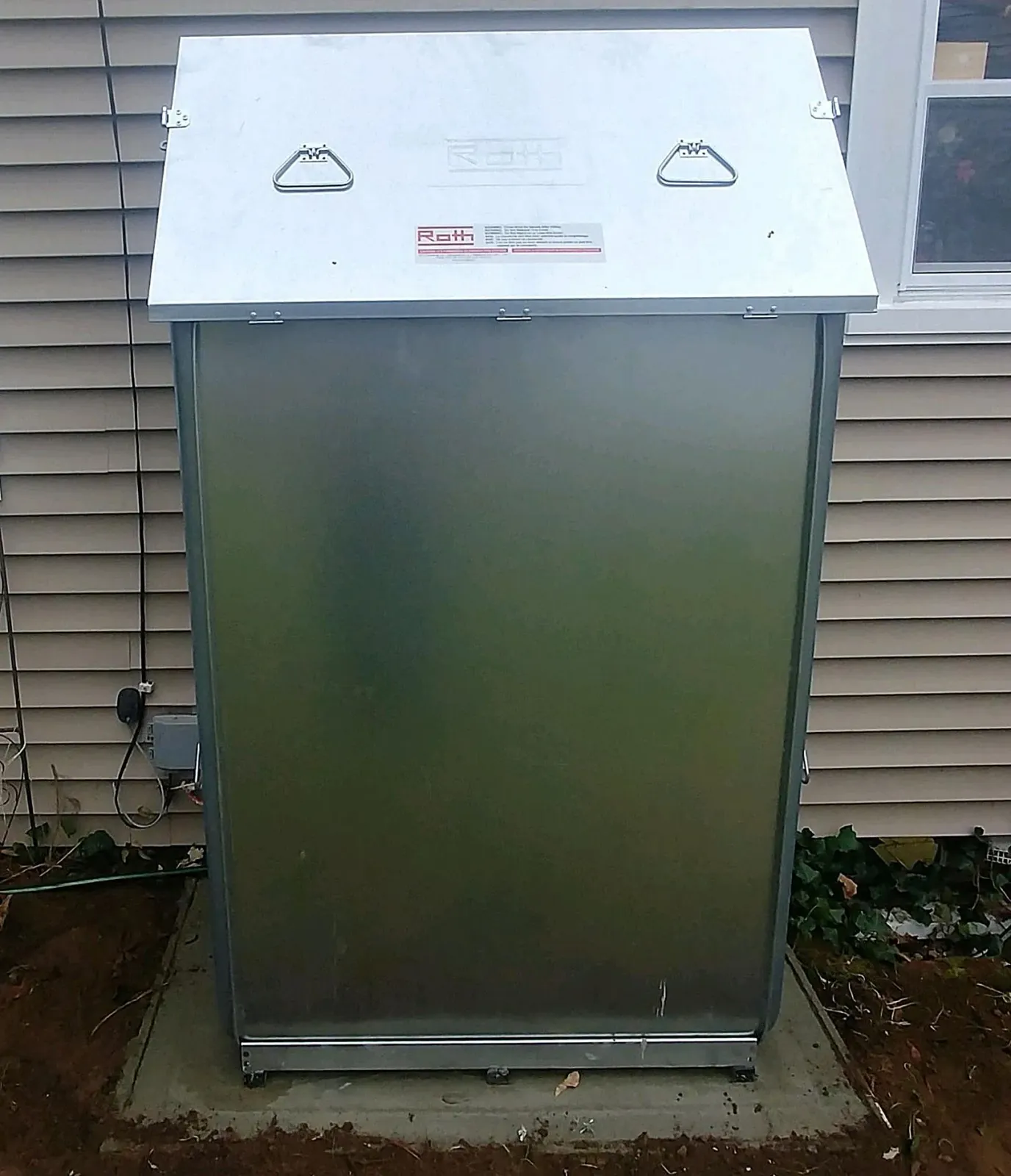 A stainless steel trash can is sitting outside of a house