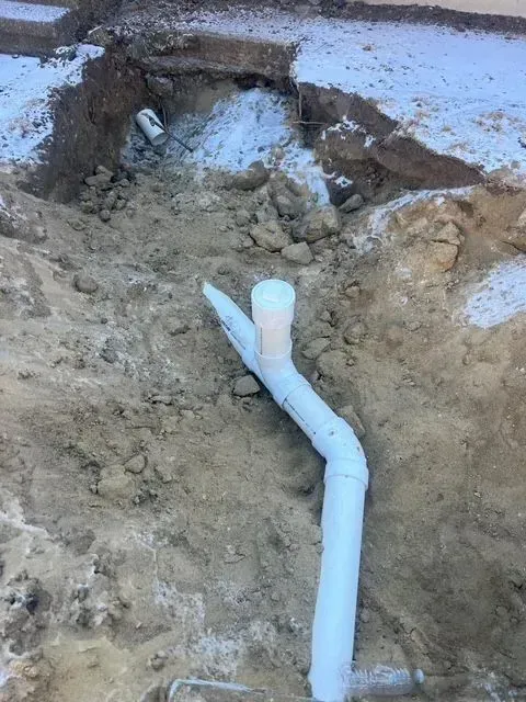 White PVC pipe emerging from a muddy trench with an open excavation around it