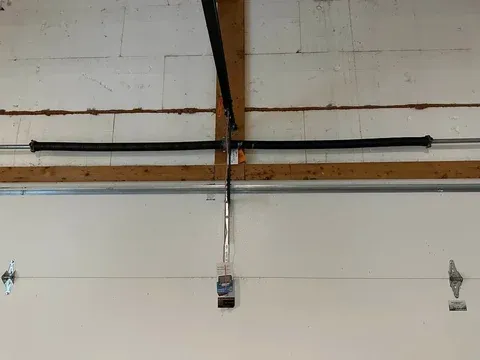 Garage door opener motor mounted on wooden beam with rails and cable system attached to white garage door panels