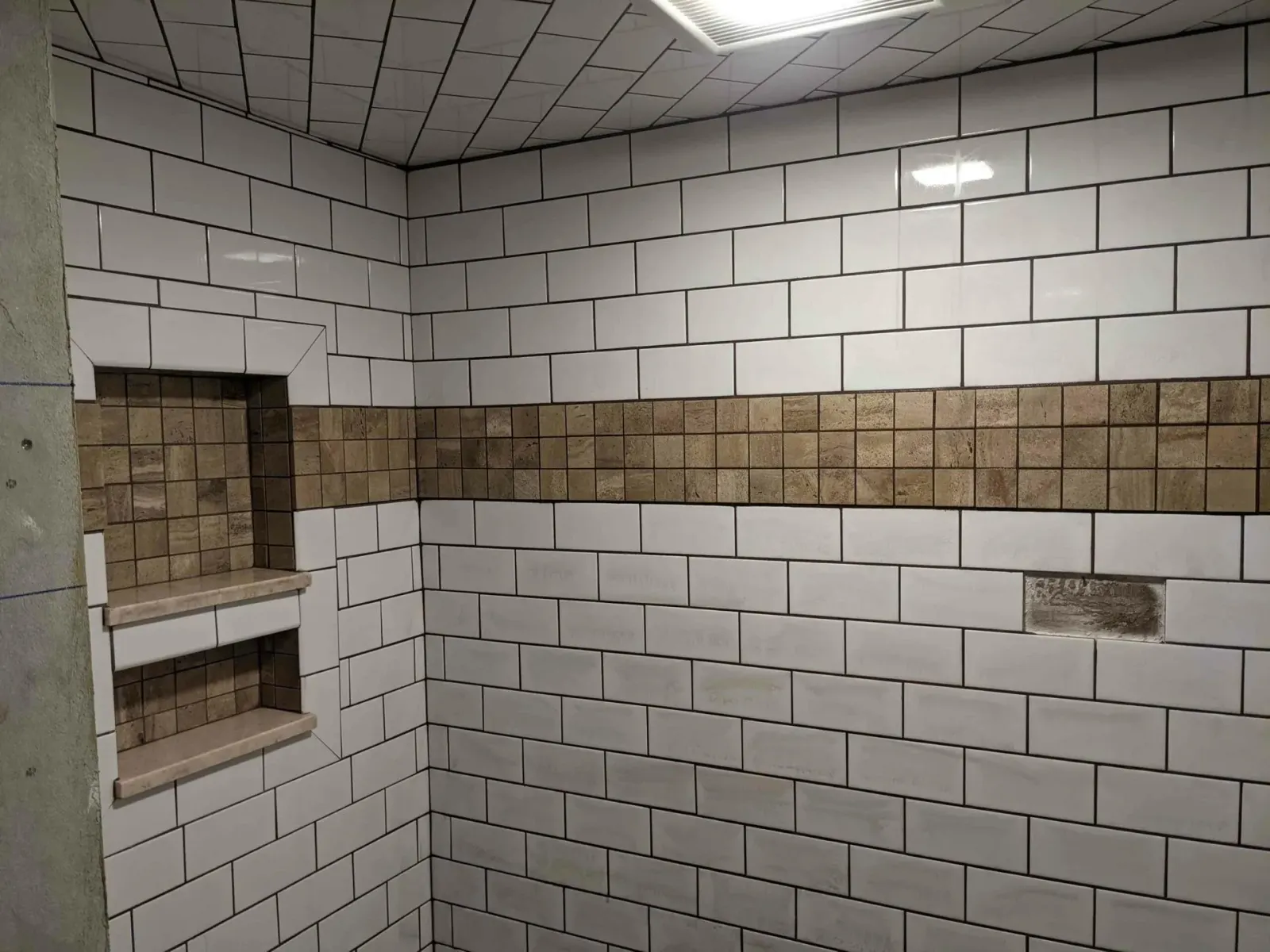 A bathroom with white tiles and a brown stripe on the wall.