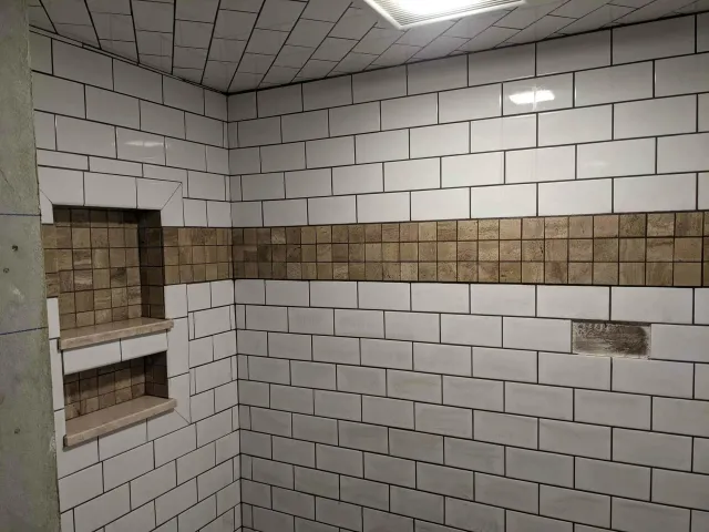 A bathroom with white tiles and a brown stripe on the wall.