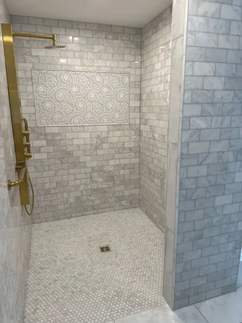 White-tiled walk-in shower with brass fixtures and mosaic floor drain.