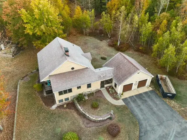 Aerial view of a two-story house with a garage, surrounded by trees and a lawn. Pathway leads to the front door.