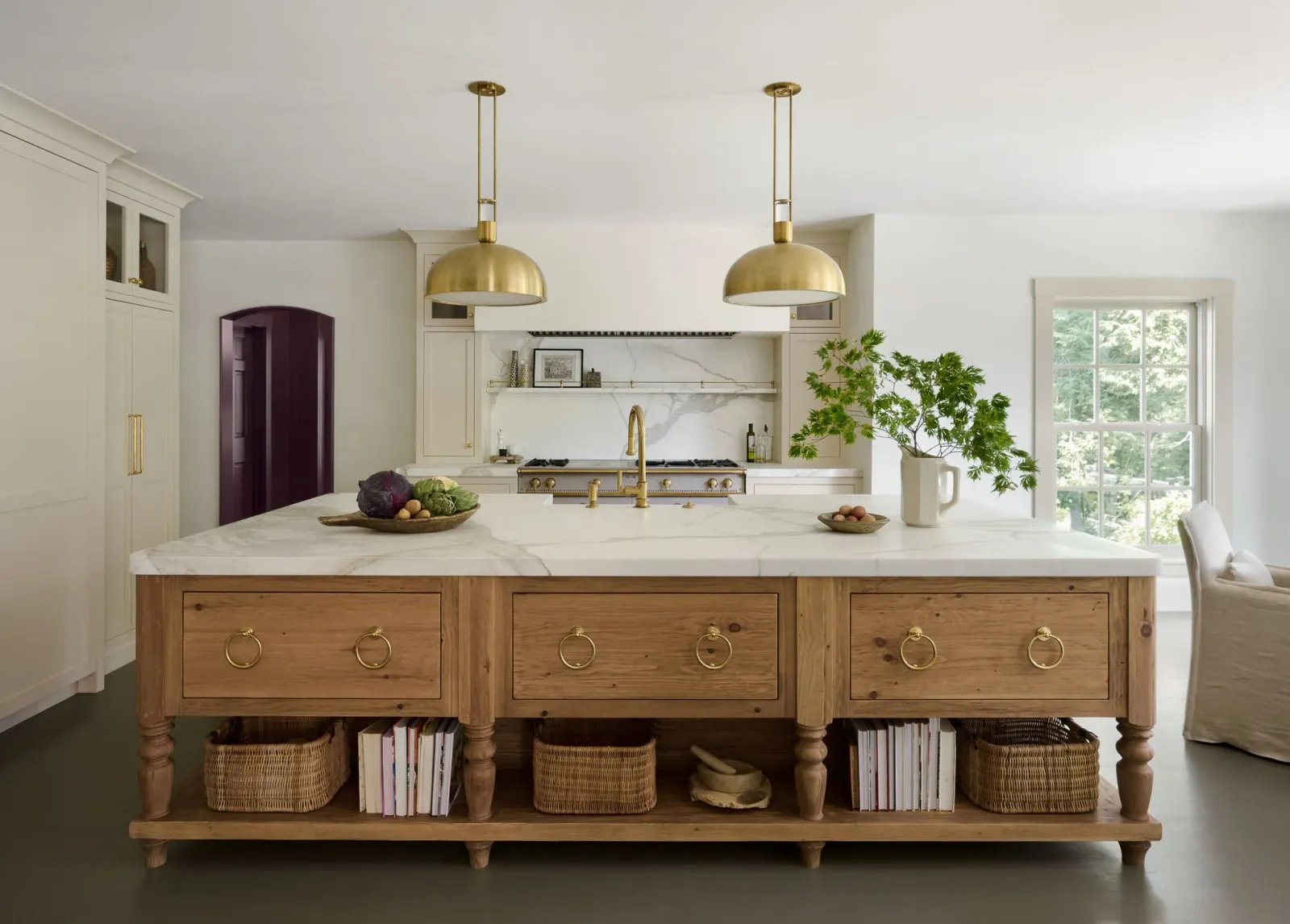 Modern kitchen with white cabinetry, marble backsplash, gold accents, wooden island with brass handles, potted plant, and natural light.