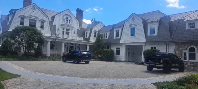 Large stone mansion with blue roof, white trim, and parked cars in a circular driveway