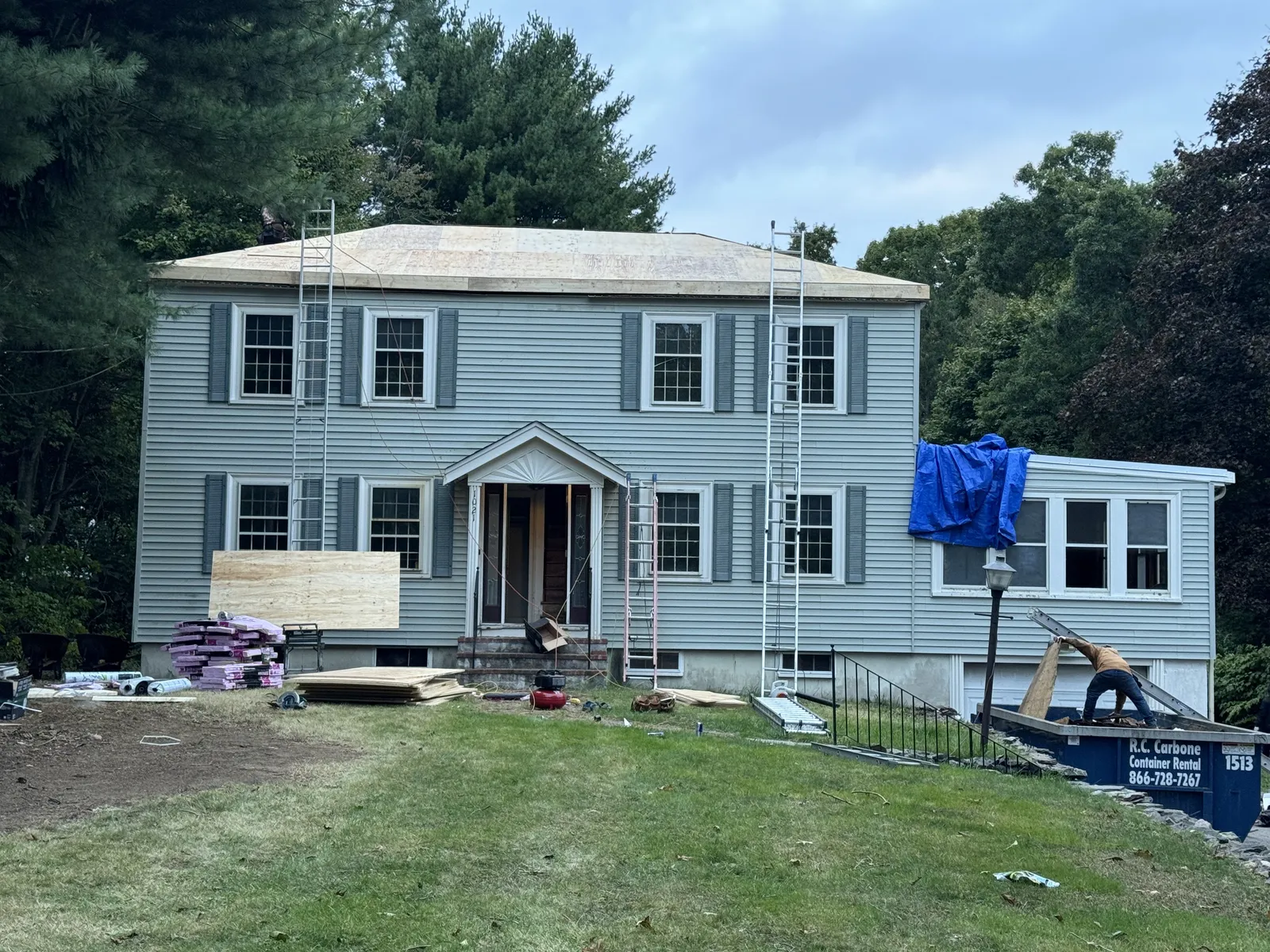 Gray colonial home in Brockton, MA mid-siding-installation with exposed sheathing and a Storm King Roofing dumpster on site