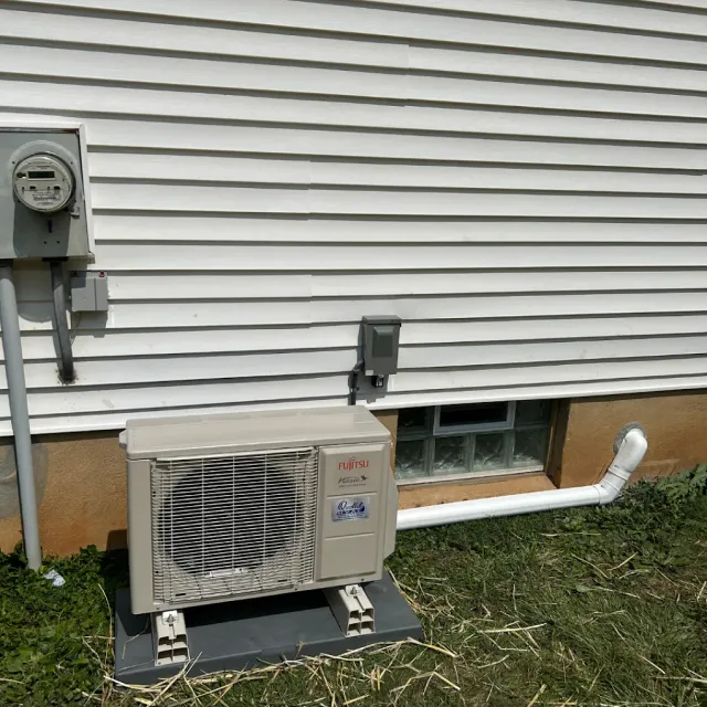 An air conditioner is sitting outside of a house next to a window.