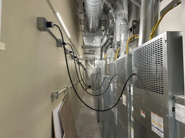 Row of mechanical units in a commercial building with conduit, boxes and receptacles run along the wall