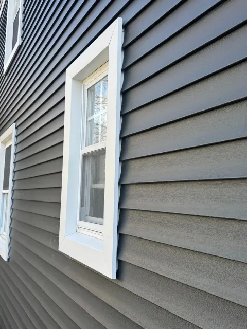 White-trimmed window on dark gray vinyl siding of a house