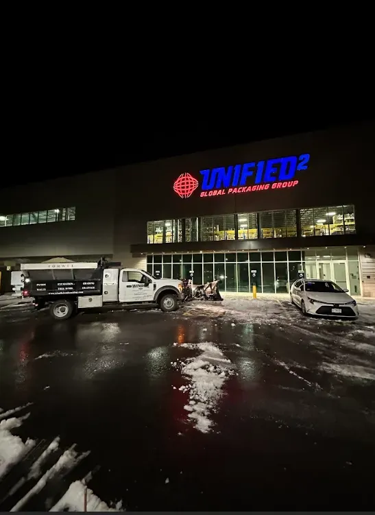 Nighttime snowy parking lot outside a UNIFIED2 building with trucks parked in front.