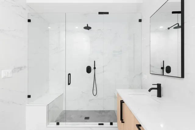 Modern bathroom installation by Dave Davidson Remodeling. White marble tile, black fixtures, light wood doors on vanity