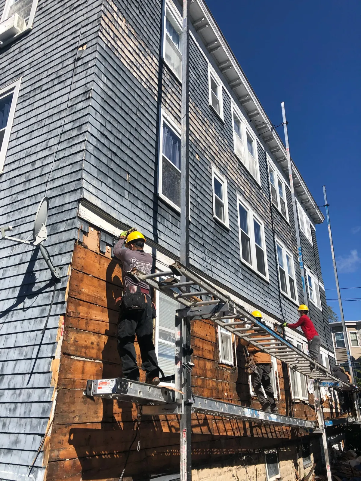 Fernandes Construction employees work to replace the shaker cedar shingles on this classic Cape Cod home