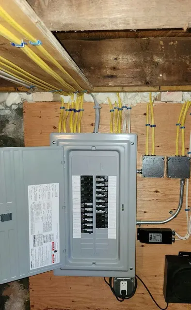 Open electrical panel in unfinished basement with exposed wiring and ductwork above.