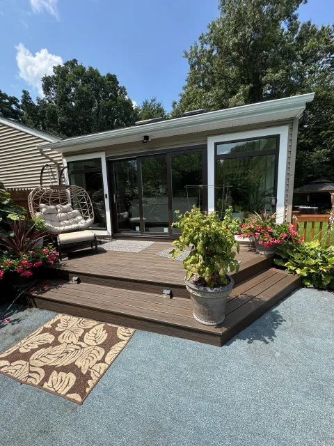 Modern garden patio with glass doors, wooden steps, potted flowers, and a patterned outdoor rug.