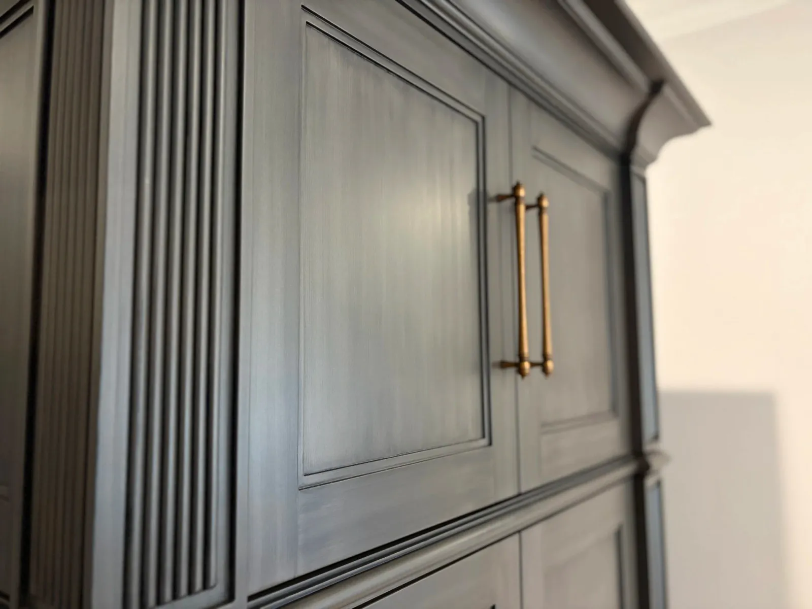 Close-up of a dark wooden cabinet with vertical ridges on the side and brass handles on the door.
