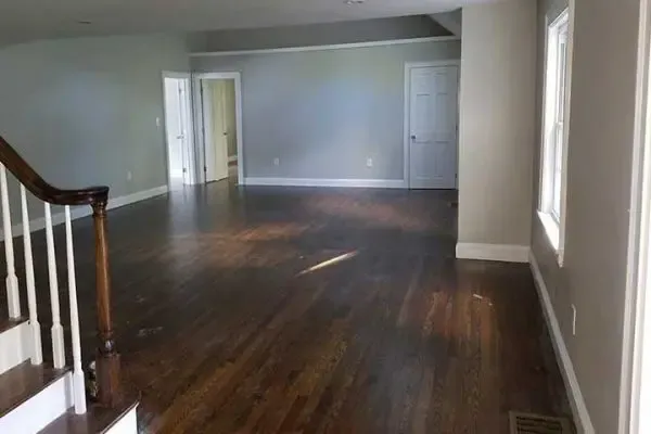 spacious, open-concept room featuring a dark-stained hardwood floor, neutral gray walls, and white trim, viewed from beside a wooden staircase bannister