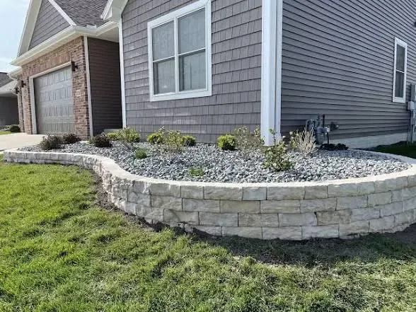 Low stone retaining wall with gravel and plants in front of a house.