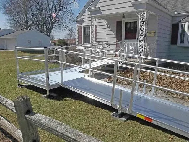White wheelchair ramp with railings leading to a house entrance on a sunny day