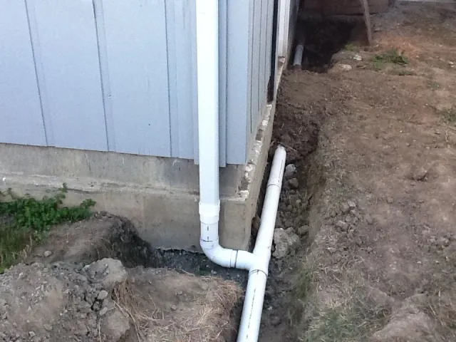PVC pipes installed along the foundation of a house, with dirt around them for drainage for gutters.
