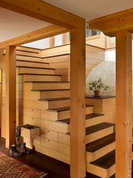 Warm Arts and Crafts interior featuring a wooden staircase with built-in drawers, dark wood treads, exposed wooden beams, and natural granite walls integrated into the design.