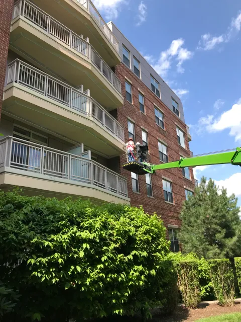 Worker on a green boom lift repairing a brick building facade near balconies.
