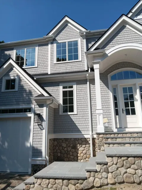 Stone-front suburban house with gray siding, white trim, and a blue sky background