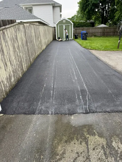 Newly paved asphalt driveway leading to a green shed; person standing near the shed.