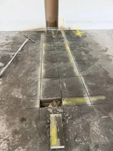 Precision slab cutting with yellow guide marks for plumbing trench access in basement