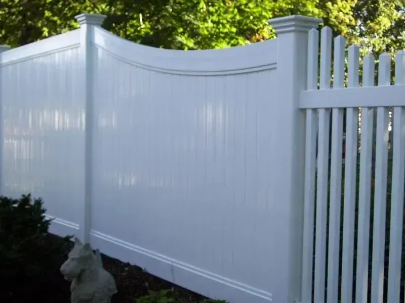 A white vinyl fence with a solid privacy panel featuring a curved top and a section of vertical pickets on the right.