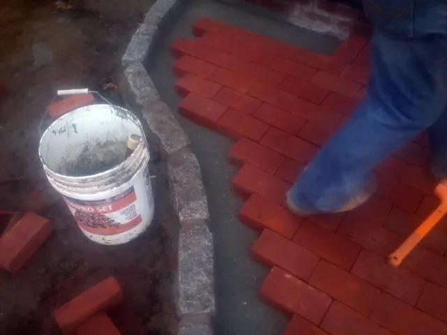 Brick paver walkway being laid against a granite cobble curb