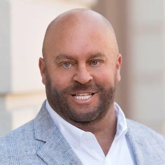 A bald man smiling in front of a building.
