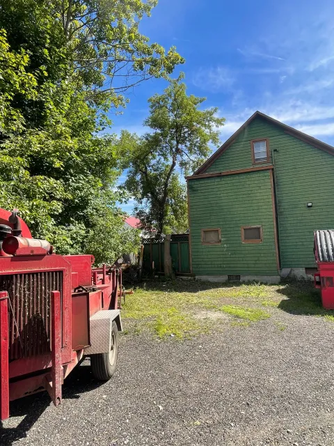 Red wood chipper next to a partially built green house with a gravel driveway, under a blue sky.