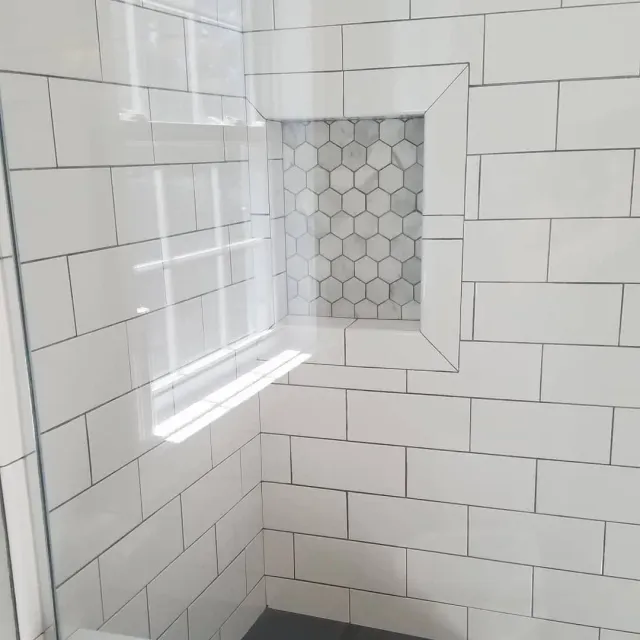 White tiled shower with hexagon accent niche and a small window.