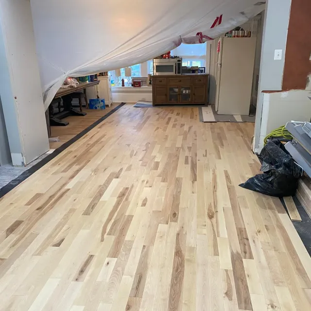 Renovated room with new light wood floor, draped plastic sheeting, and furniture covered at the back.