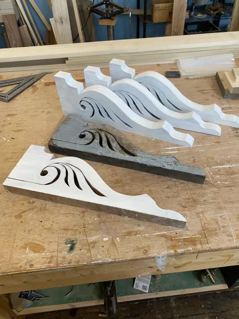 Wooden woodworking project pieces with carved wave and swirl design, on a workbench in a workshop.