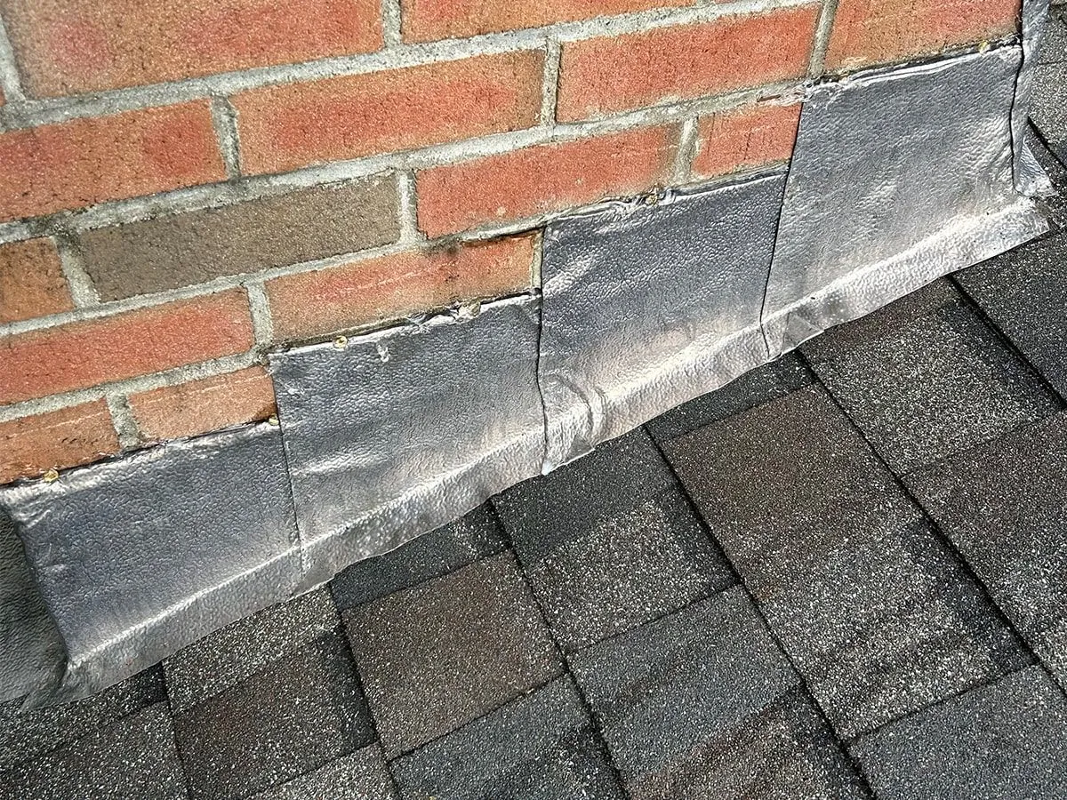 Brick wall above a dark shingled roof with gray flashing at the base