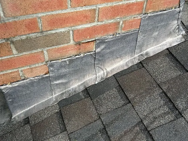 Brick wall above a dark shingled roof with gray flashing at the base