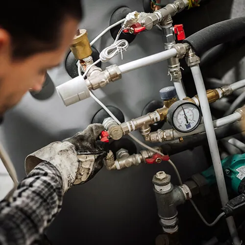Technician wearing gloves adjusting valves on gas line pipes with a pressure gauge.