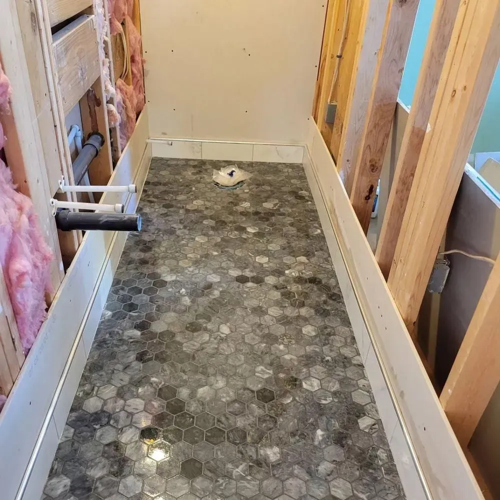 Narrow unfinished bathroom with tiled floor, exposed wall framing, and plumbing during renovation