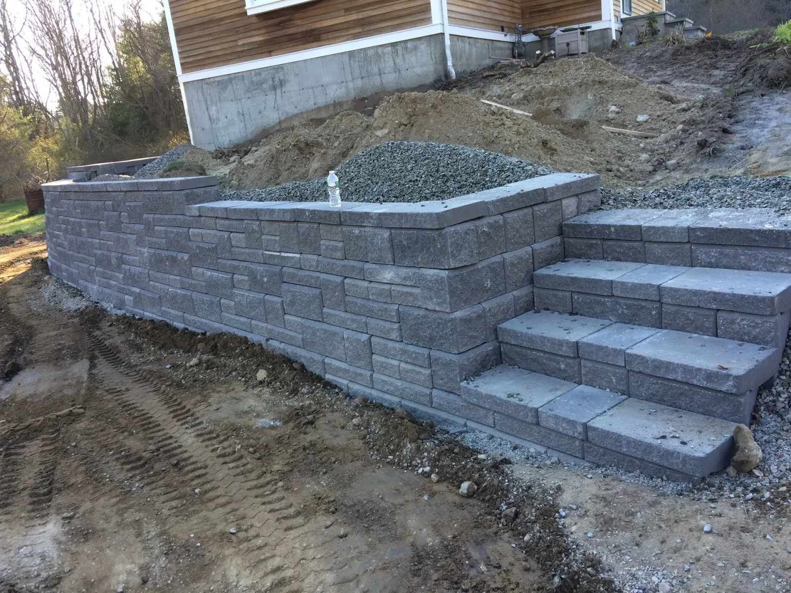 Stone retaining wall and steps built into a hillside, next to a house under construction.