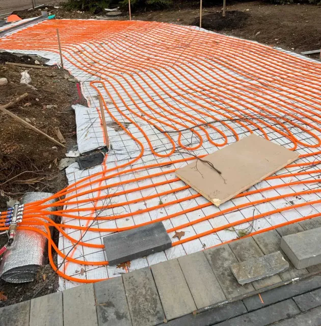 Orange radiant heating tubes laid out on a concrete base.