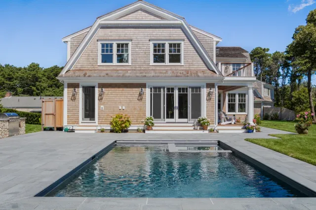 Elegant gabled shingle house with sparkling swimming pool and stone patio.