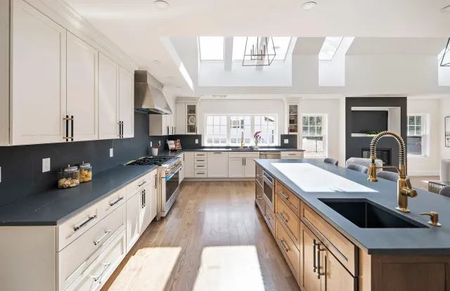 Modern kitchen with white and wooden cabinets, black countertops, stainless steel appliances, and large skylights.