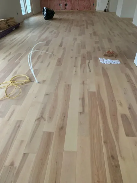Empty room with light wood flooring, loose cables, and construction materials near the far wall.