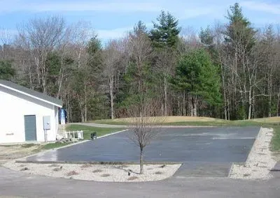 A parking lot with a white building in the background and trees in the background