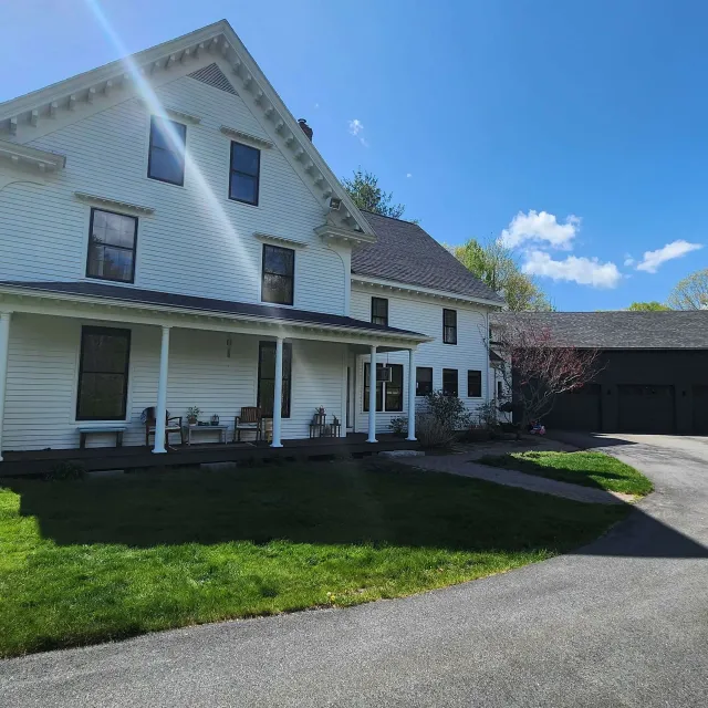 White Victorian-style house with porch, green lawn, driveway, and blue sky on a sunny day